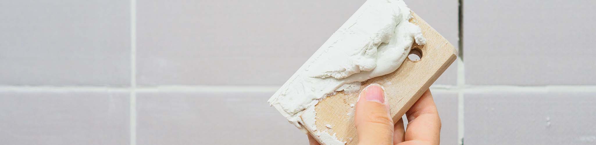 Grouting between tiles in the bathroom. Female hand holds a spatula. Repairs.